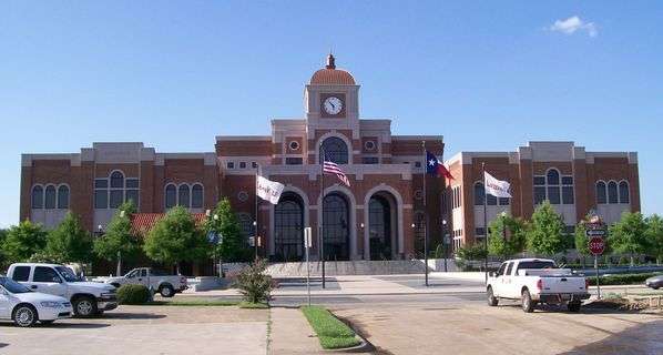 Large brick municipal-looking building with parking lot in front, in Lewisville, TX.