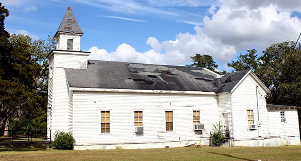 A white church in Corinth, TX, with trees and blue sky behind it.