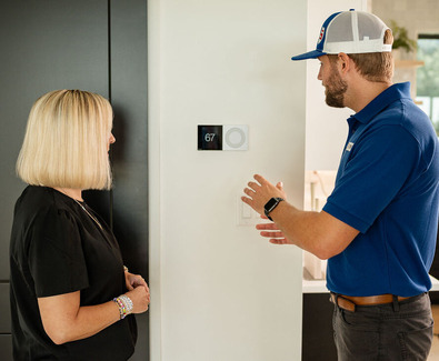 Technician speaking with a homeowner about her new thermostat installed on a white wall.