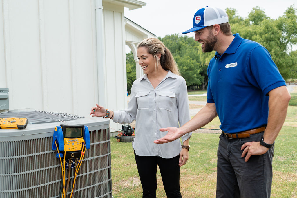 Technician showing HVAC unit to homeowner outside a white home.