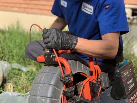 Plumber performing sewer line repair outside a brick home.
