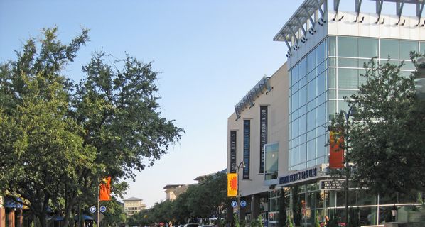 View of a city street with tall buildings to the right and trees to the left.