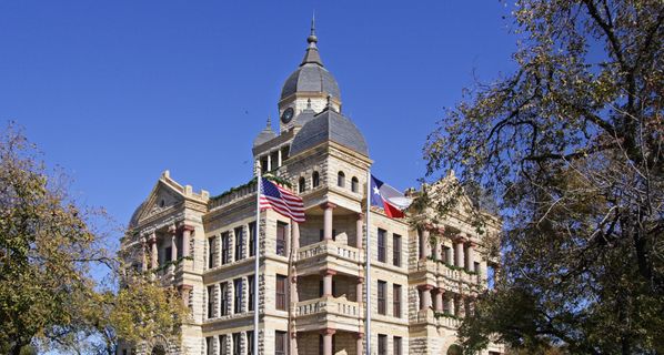 Large stone city-hall-style building with blue sky in background and trees on either side.