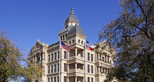 Large stone city-hall-style building with blue sky in background and trees on either side.