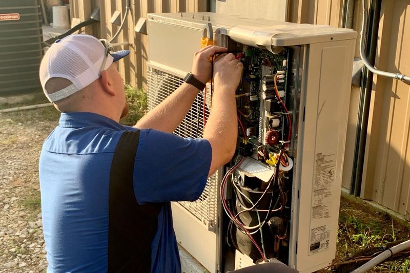 Technician performing AC repair on a unit next to a home.