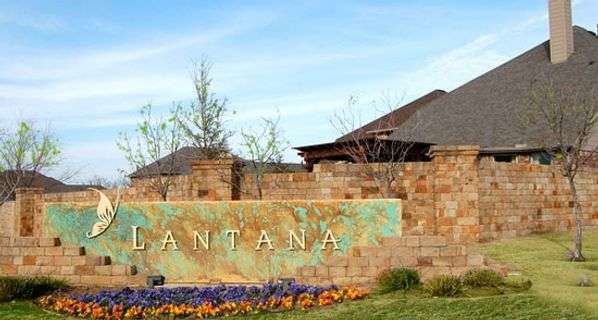 Stone wall with purple and orange flowers along ground in front. Part of wall is a sign that says "Lantana"