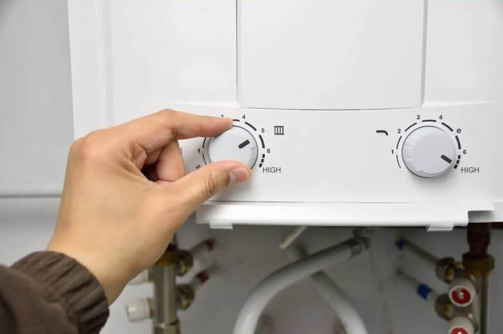  Woman's hand adjusting a knob on a tankless water heater. 