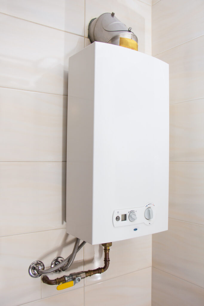 Tankless water heater mounted on a white tile bathroom wall in a Dallas home.