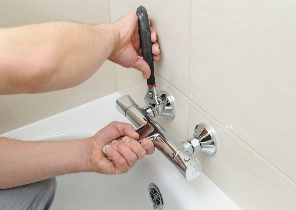 Close view of a plumber's hands as they use a tool to repair a bathtub faucet.