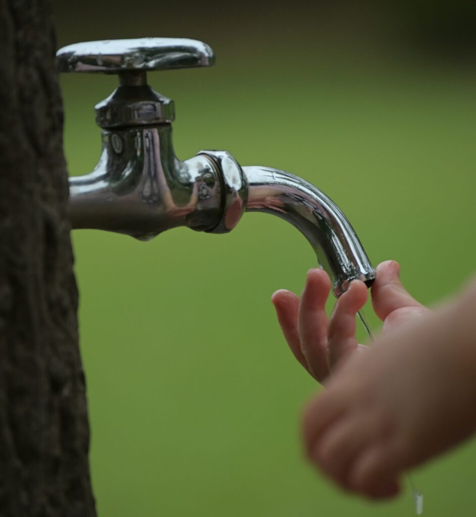 Close view of a child's hand under a running outdoor faucet.